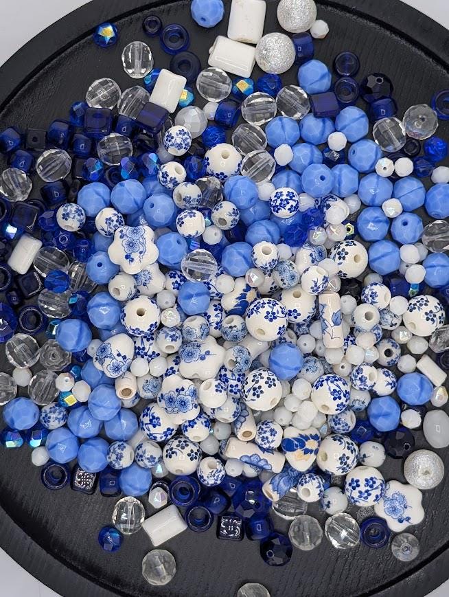 The image is a collection of various beads and beads in shades of blue and white, scattered on a black surface.