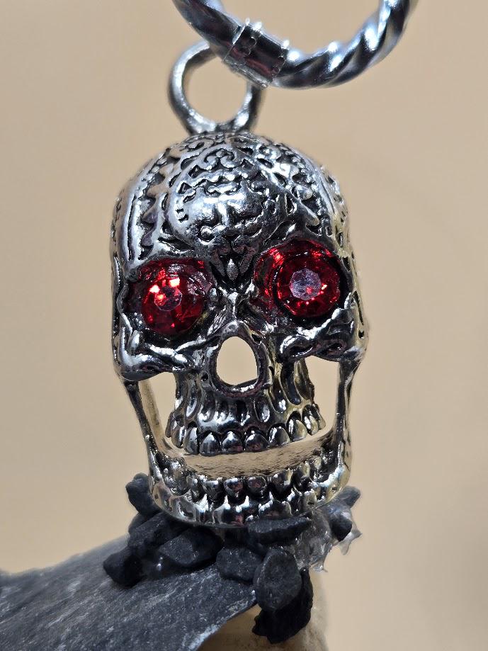A silver skull pendant with red gemstones, hanging from a chain.