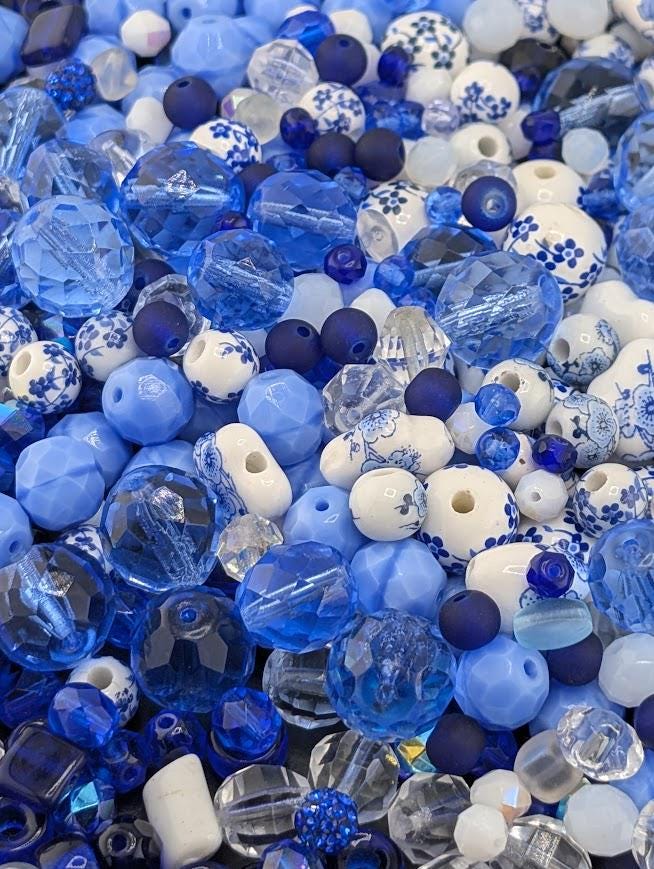The image is a close-up of various blue and white beads, glass beads, and crystal beads, creating a visually appealing and colorful arrangement.