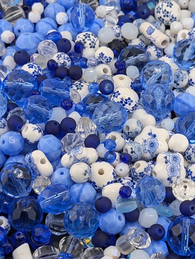 The image is a close-up of various blue and white beads, including clear and white beads, as well as blue and white beads with floral designs. The beads are scattered throughout the frame, creating a visually appealing and colorful composition.