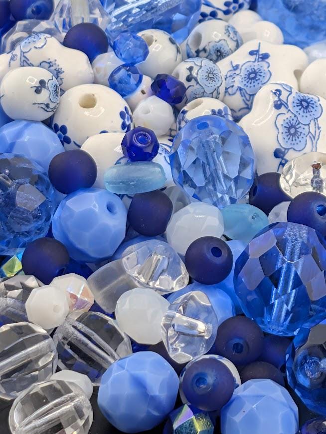 The image is a collection of various blue and white beads, including clear and blue glass beads, arranged in a visually appealing manner.