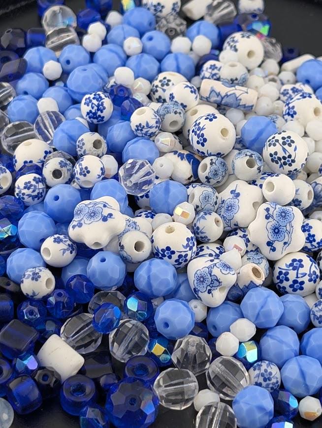The image is a close-up of various beads and beads in shades of blue and white, with some clear beads mixed in.