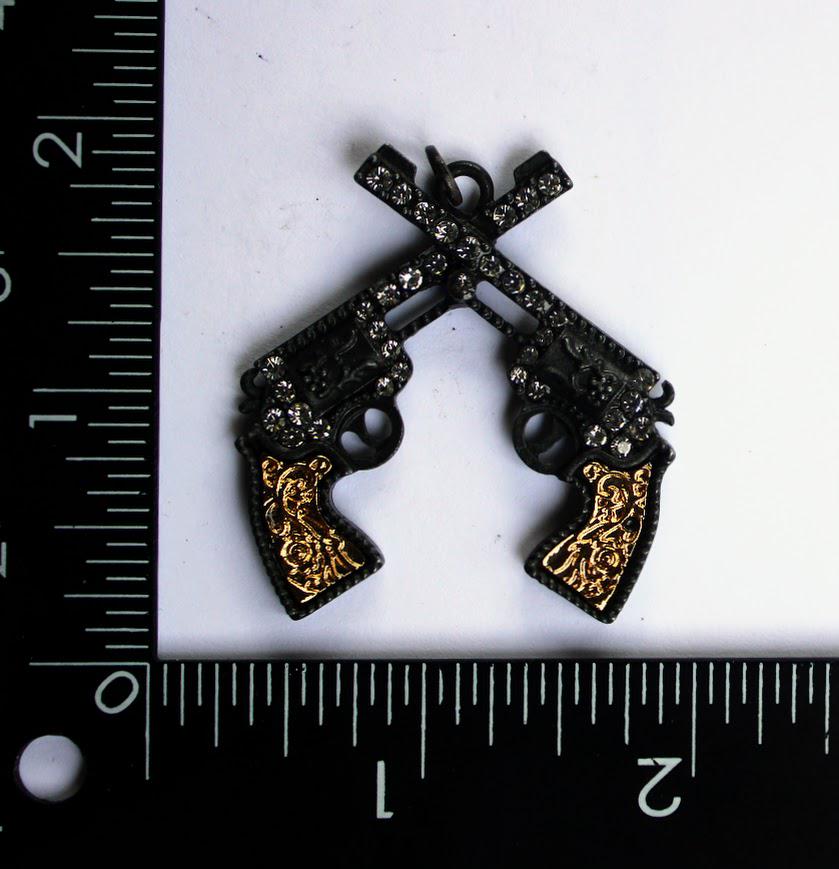 A black and gold ornate gun clasp with crossed handles, placed next to a ruler for scale.