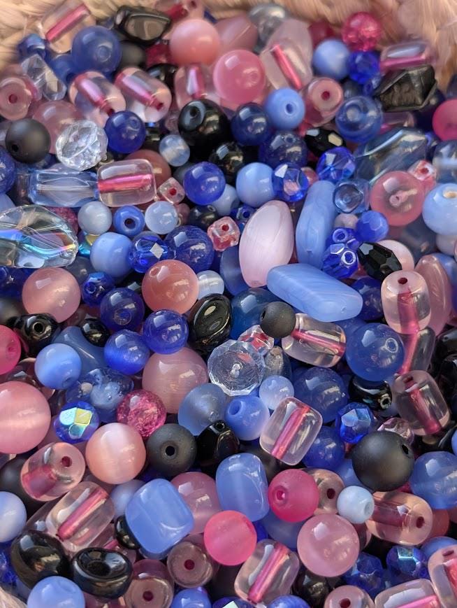 The image is a close-up of a collection of colorful beads, including clear, blue, pink, and black beads, as well as some multicolored beads.