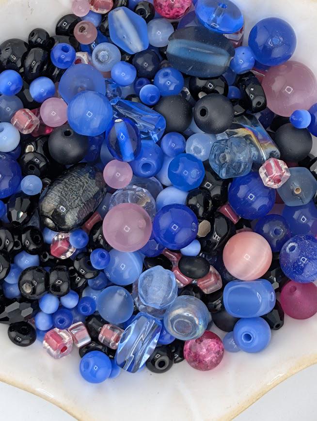 A white bowl filled with a variety of colorful glass beads in shades of blue, black, and pink.