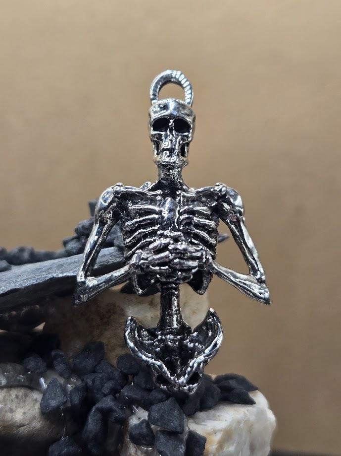 A silver-colored metal skeleton pendant is displayed against a beige background.