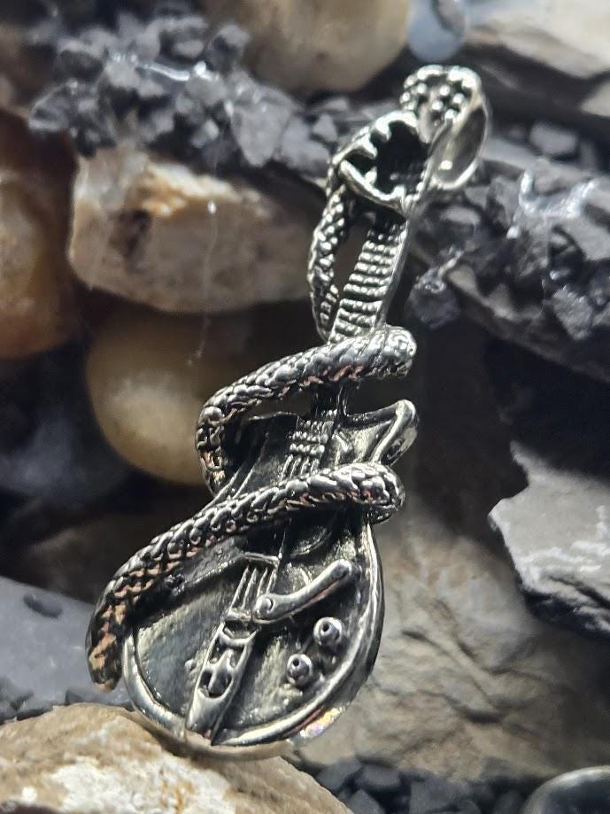 A silver-colored pendant in the shape of a guitar with a snake wrapped around it, resting on a bed of rocks.