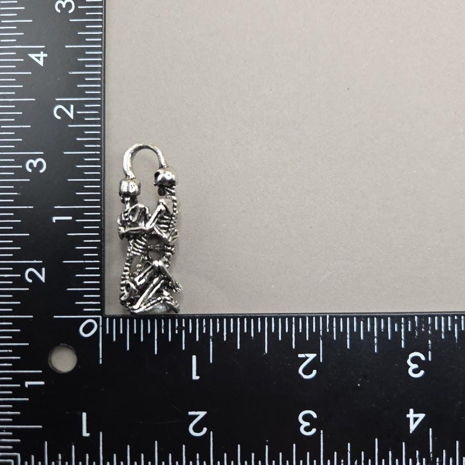 A silver-colored metal charm or pendant is placed next to a ruler, indicating its size.