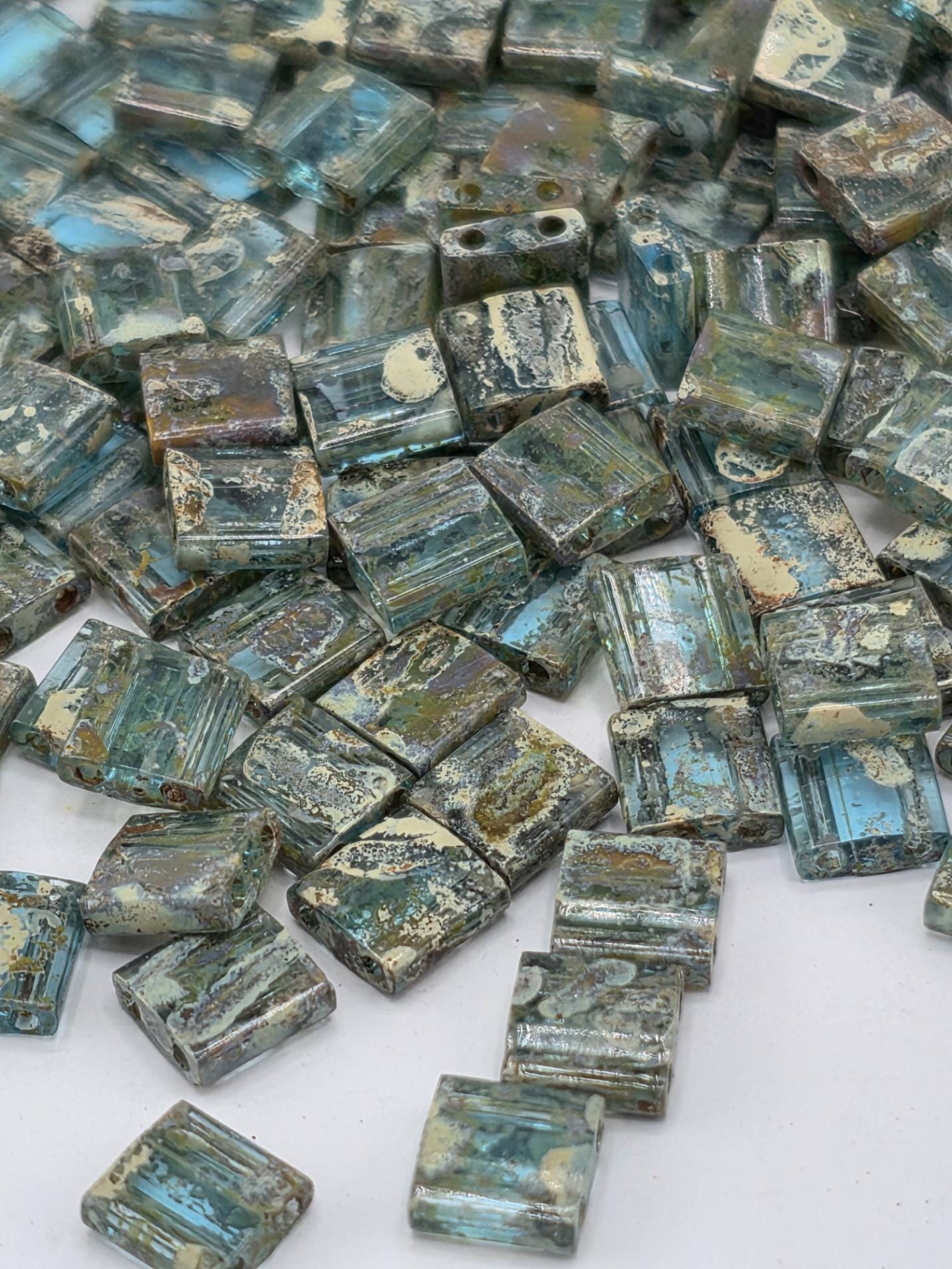 a collection of small, square-shaped blue and green glass beads scattered on a white surface.