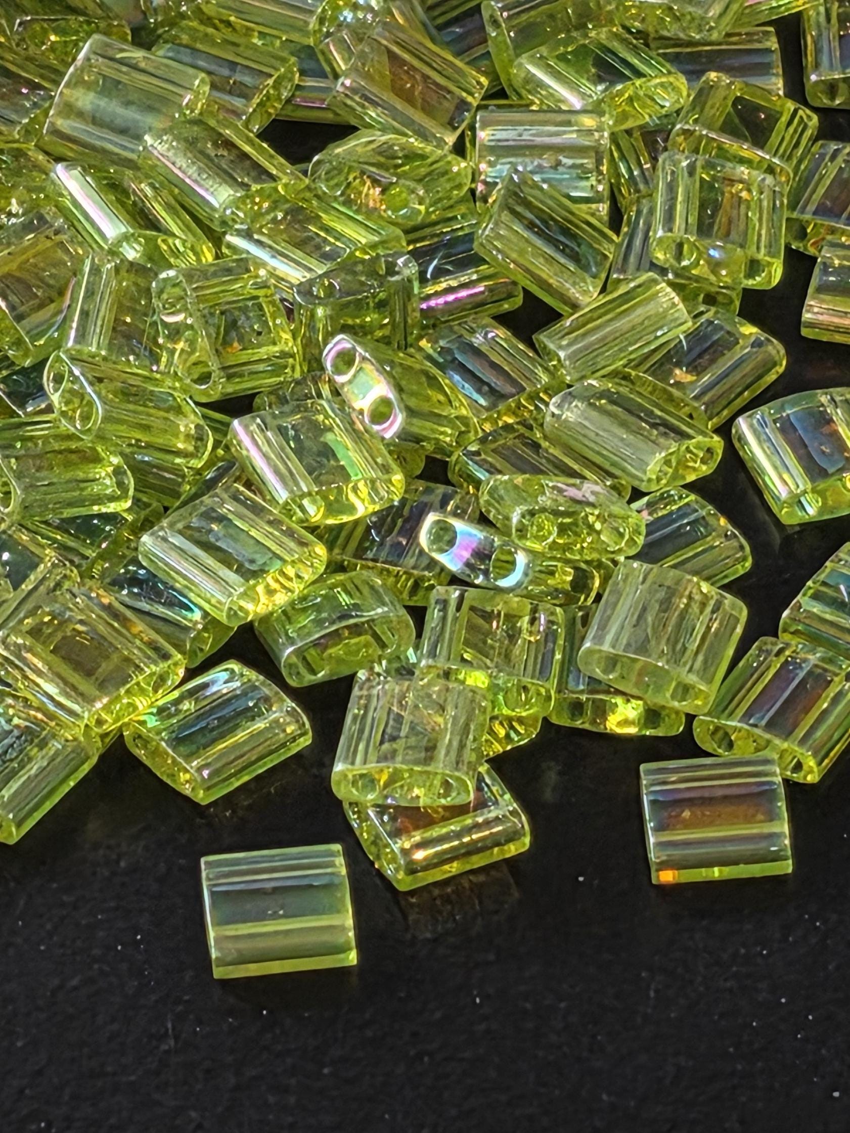a close-up view of numerous small, clear, and shiny green glass beads scattered on a dark background.