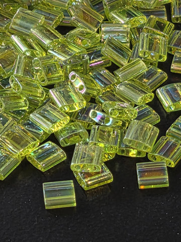 a close-up view of numerous small, clear, and shiny green glass beads scattered on a dark background.