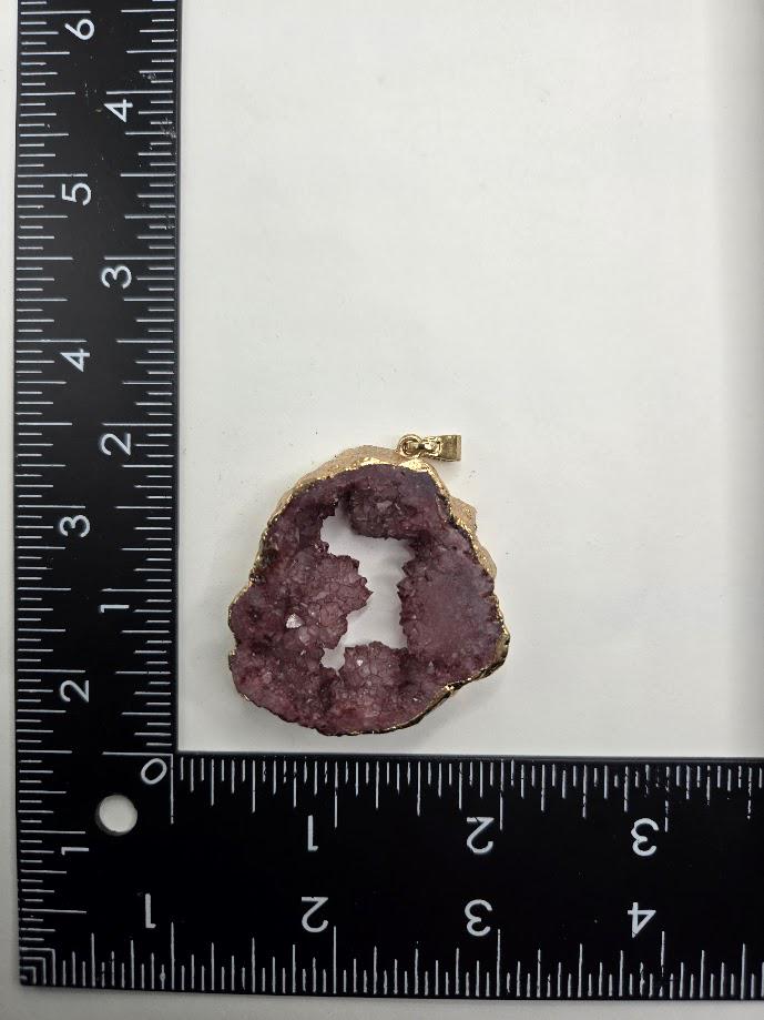 a large purple gemstone with a gold-colored cut, placed next to a ruler for size comparison.