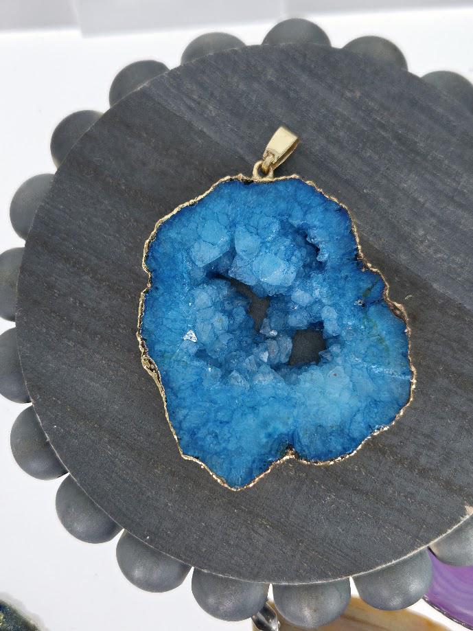 A large, blue geode-like stone with a gold-colored border is displayed on a gray wooden stand.