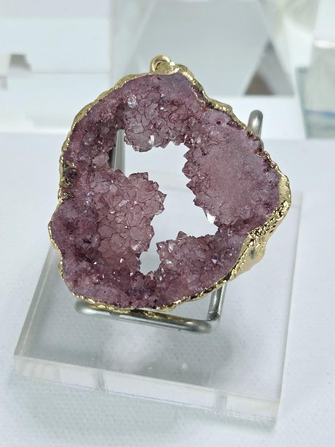 a large, purple-colored rock with a gold-colored interior, displayed on a clear stand.