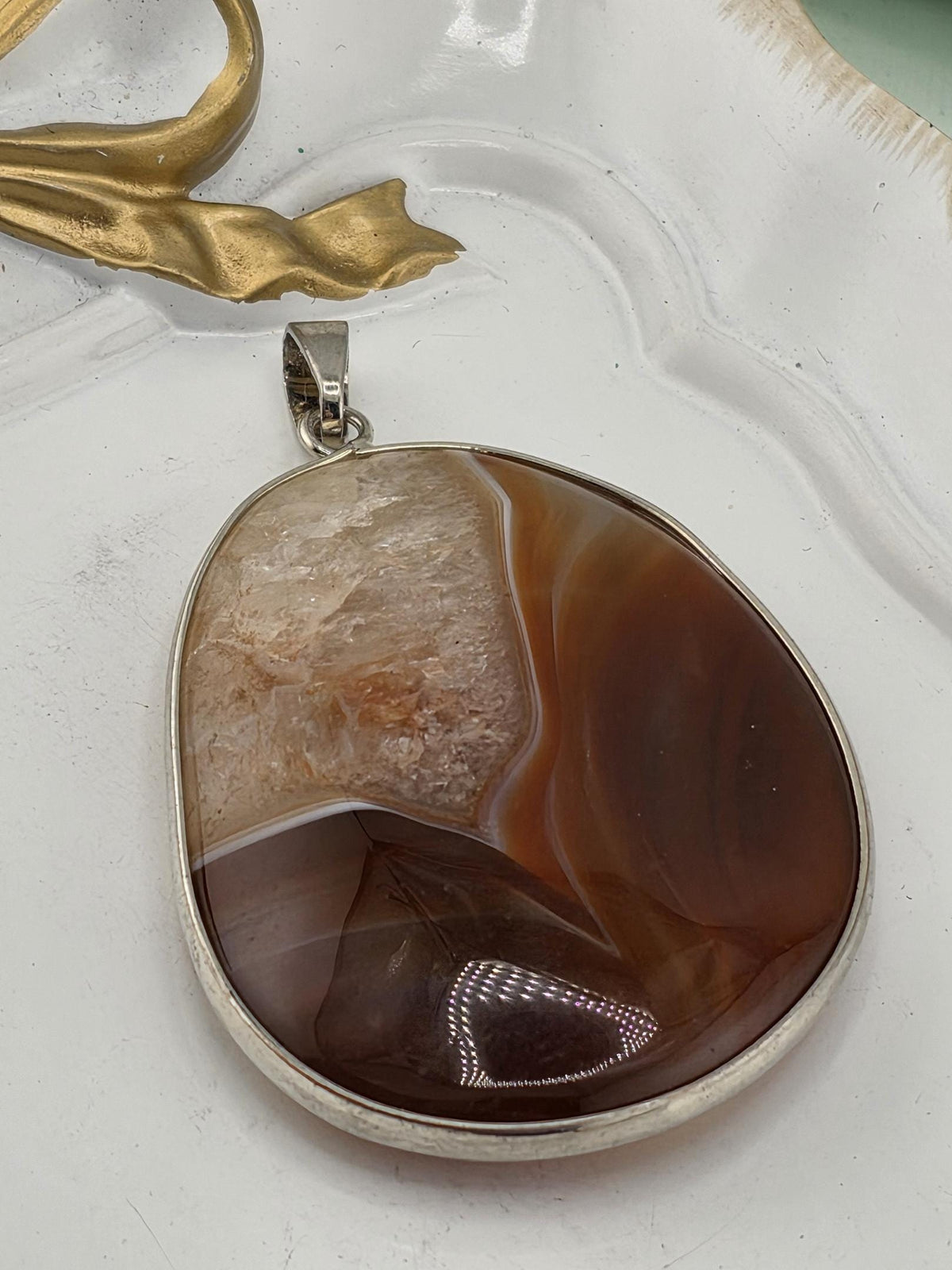 a large, oval-shaped stone with a unique, multicolored pattern, possibly a piece of natural rock or gemstone. The stone is attached to a silver-colored pendant or charm, which is hanging from a chain or cord.