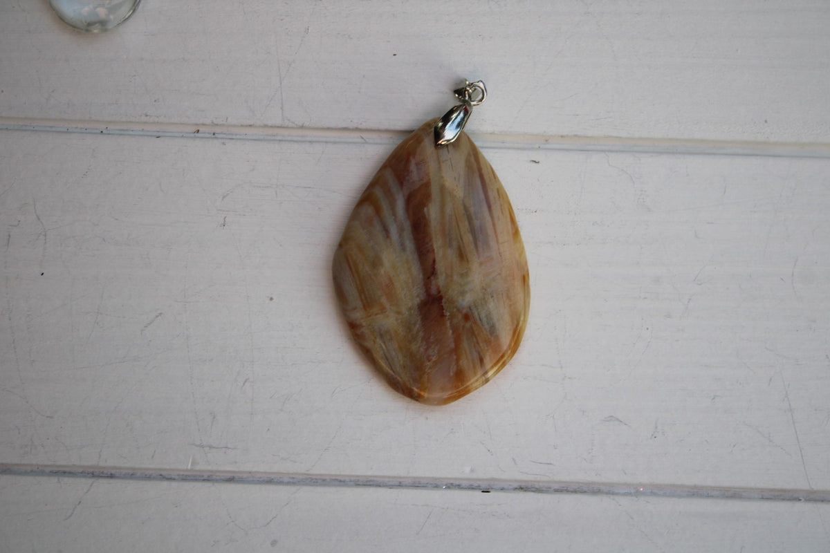 A pendant made of a brownish-orange stone is hanging on a white wooden surface.
