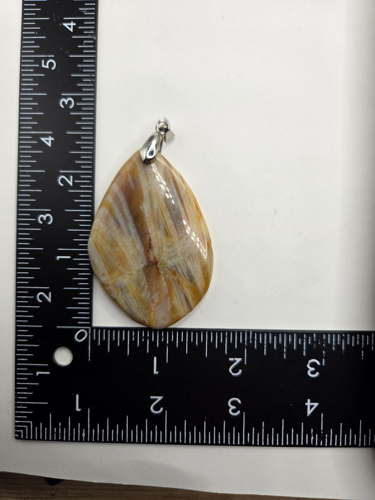 a pendant with a unique, irregular shape resting on a ruler for size comparison.
