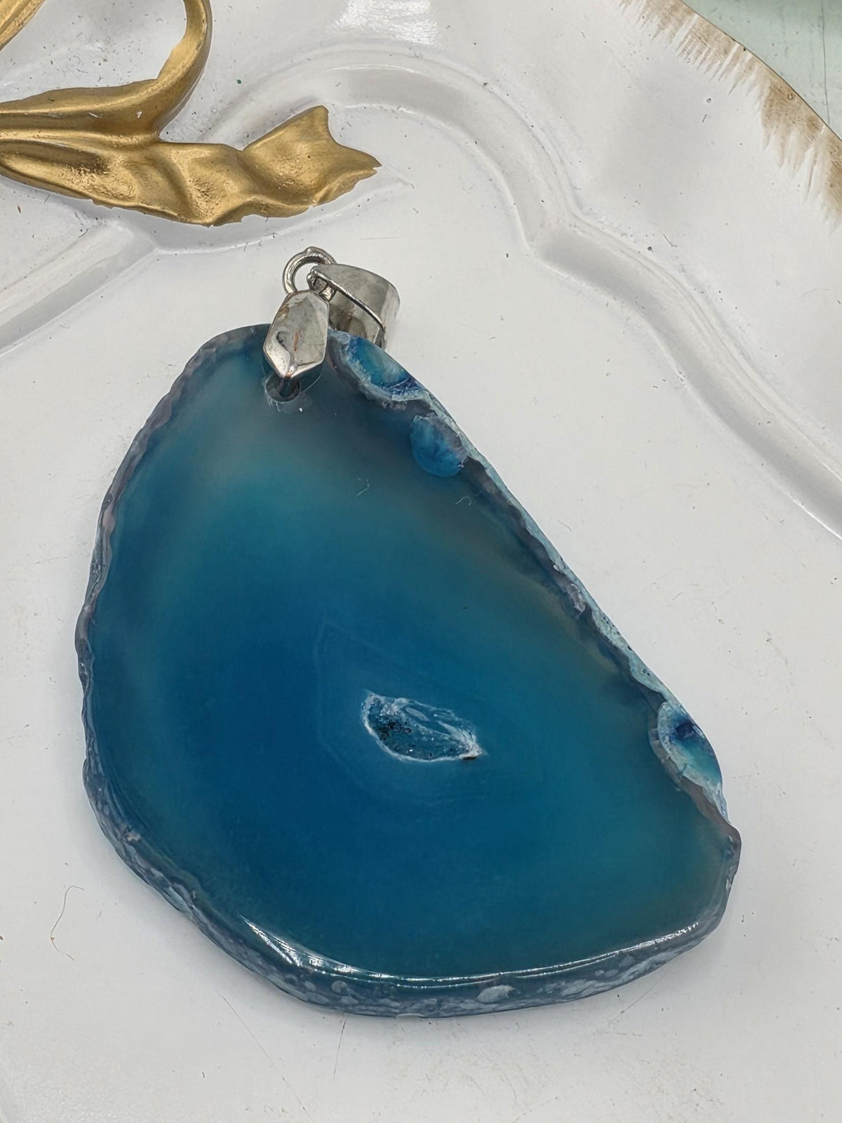 A blue agate stone with a small hole in the center, placed on a white surface.