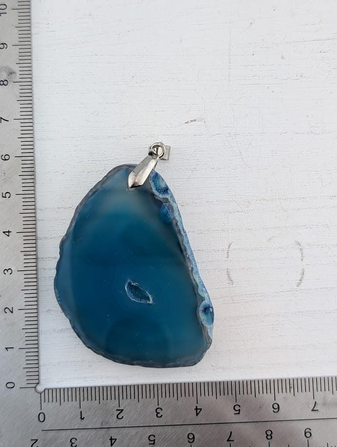 A blue agate stone with a silver clasp is placed on a white surface, with a ruler for scale.