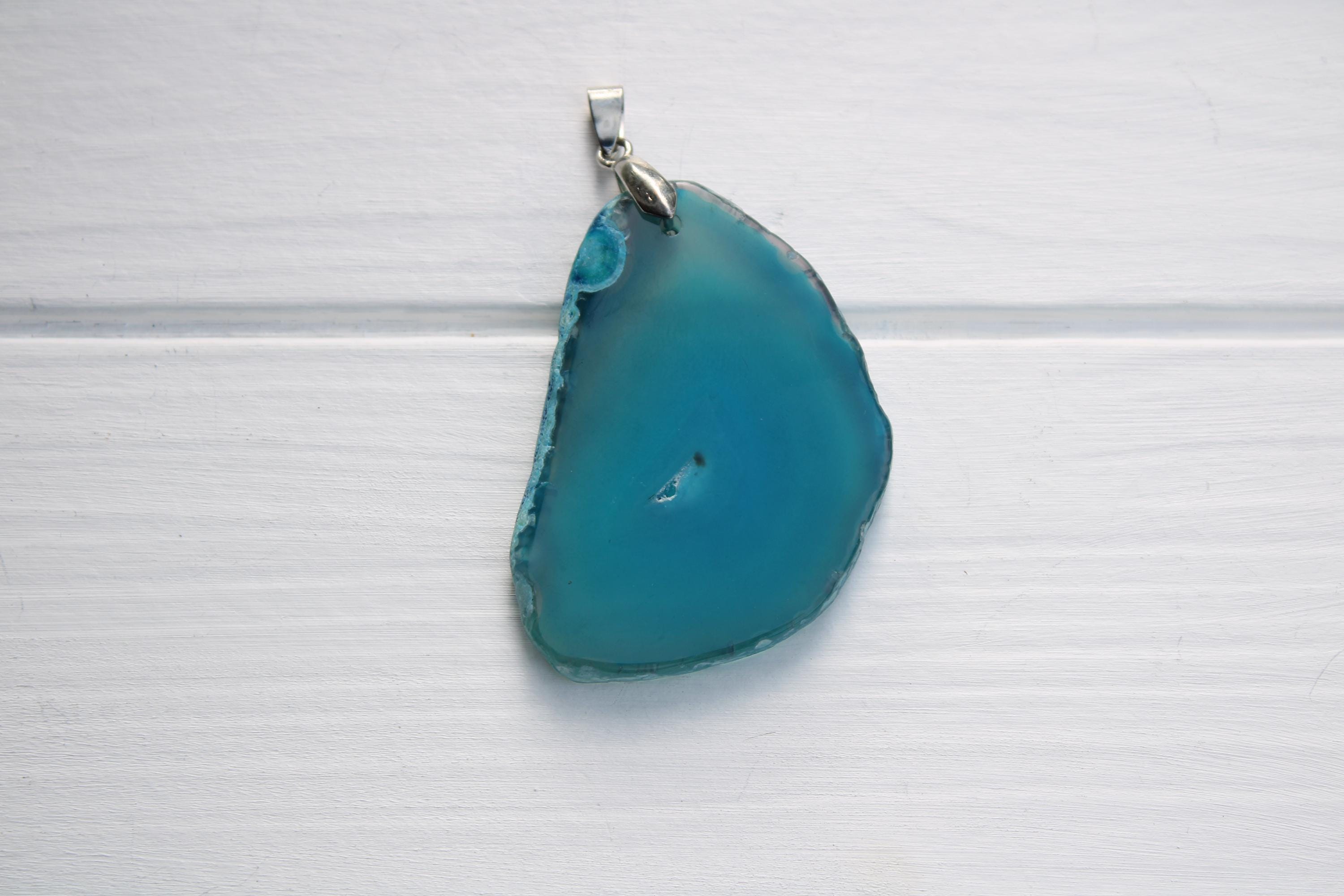 A piece of blue-green stone, possibly a gemstone, is hanging from a silver chain against a white background.