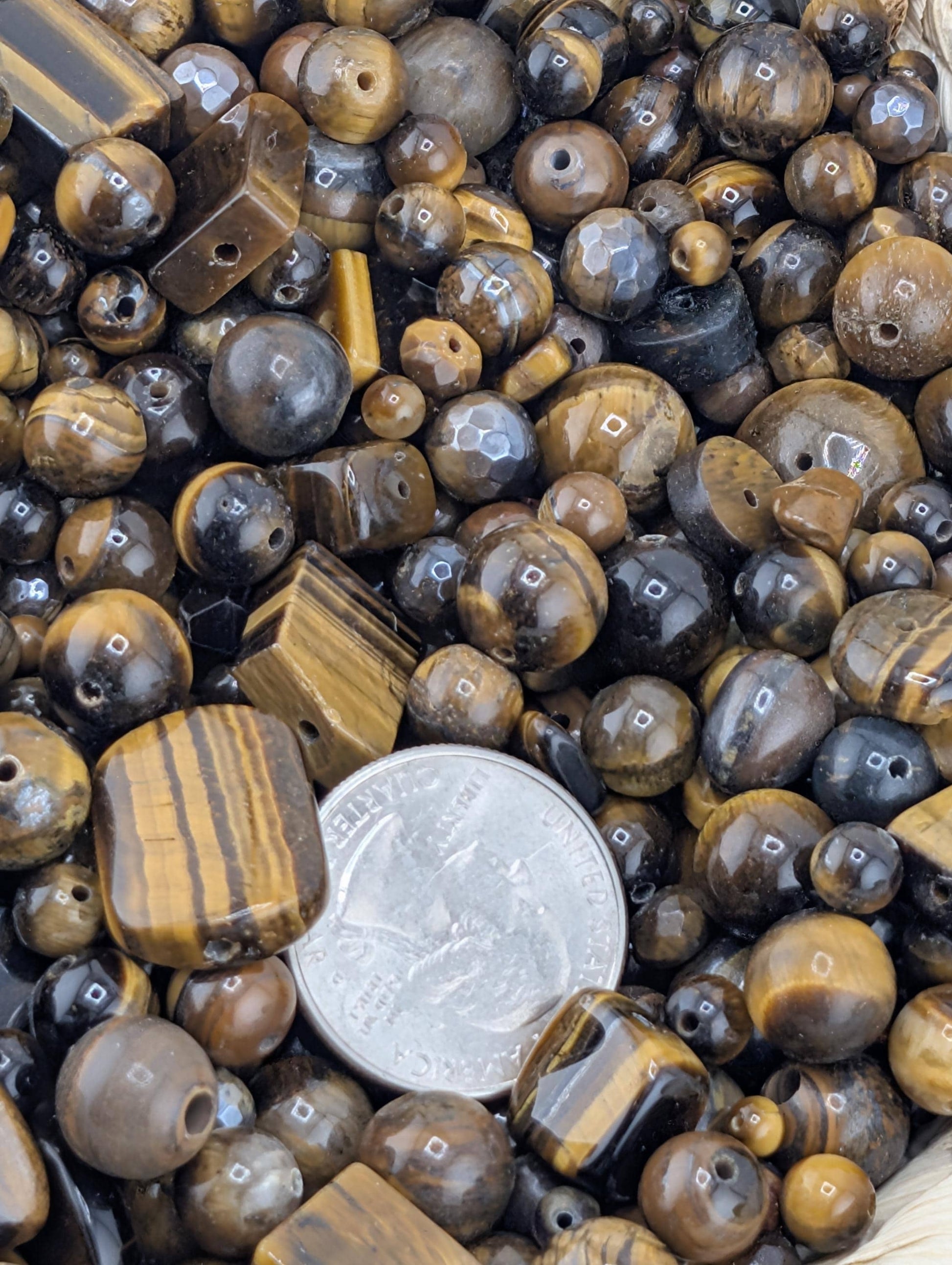 a collection of various beads, including tiger eye beads, scattered together. A quarter is placed on top of the beads, which is a notable object among the collection.