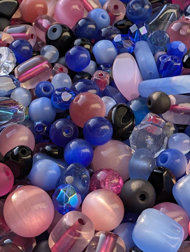 The image is a close-up of a collection of colorful glass beads, including various shades of blue, pink, and purple.