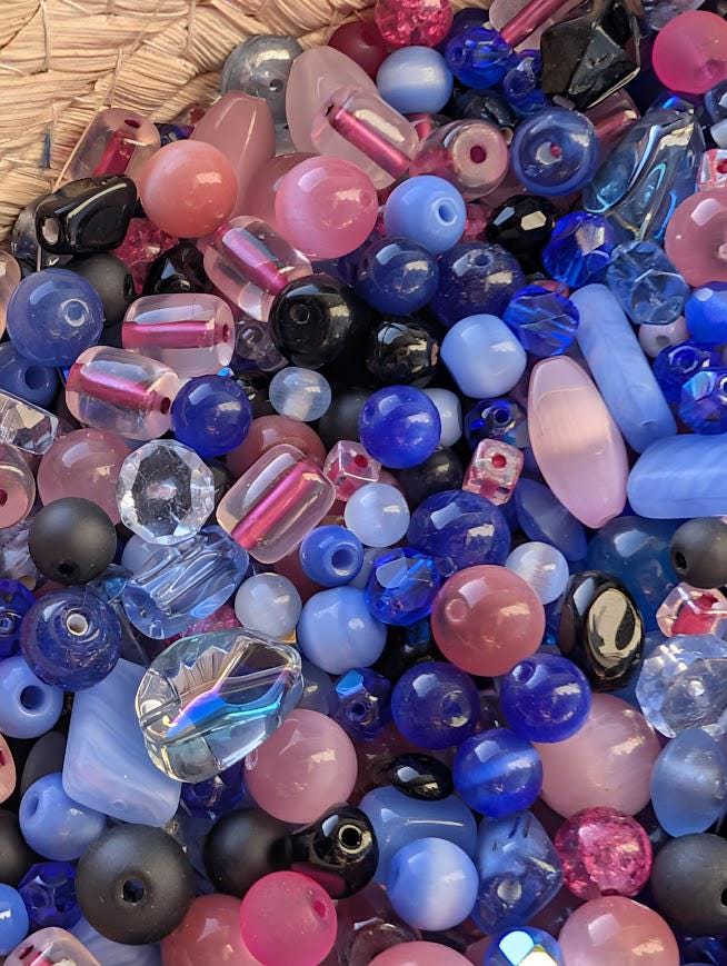 The image is a colorful assortment of various beads, including clear, blue, pink, and black beads, as well as some that appear to be made of glass or crystal.
