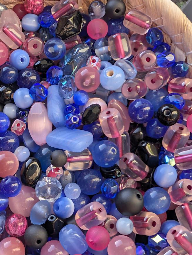 The image is a close-up of a variety of colorful beads, including clear, blue, pink, and black beads, arranged in a visually appealing manner.
