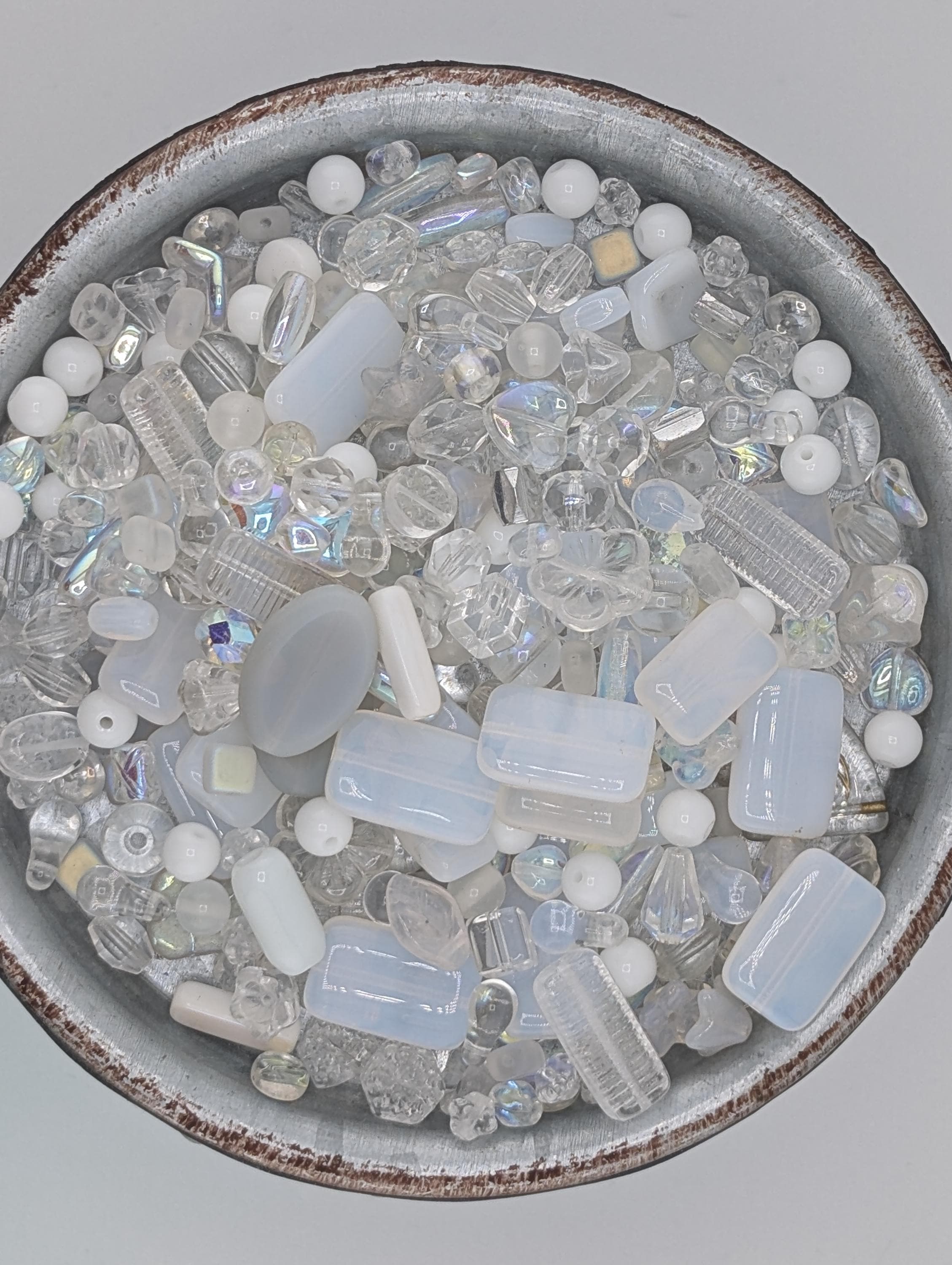 A bowl filled with various clear glass beads in different shapes and sizes, creating a visually appealing and diverse collection.