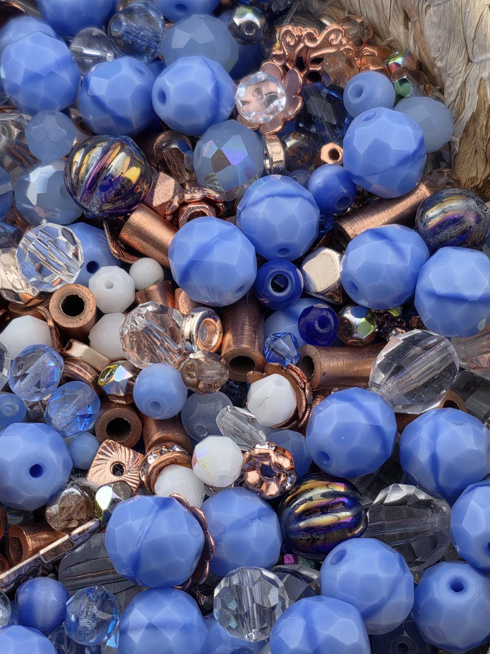 The image is a close-up of various blue and copper-colored beads, including clear and multicolored beads, as well as some copper-colored metal pieces.