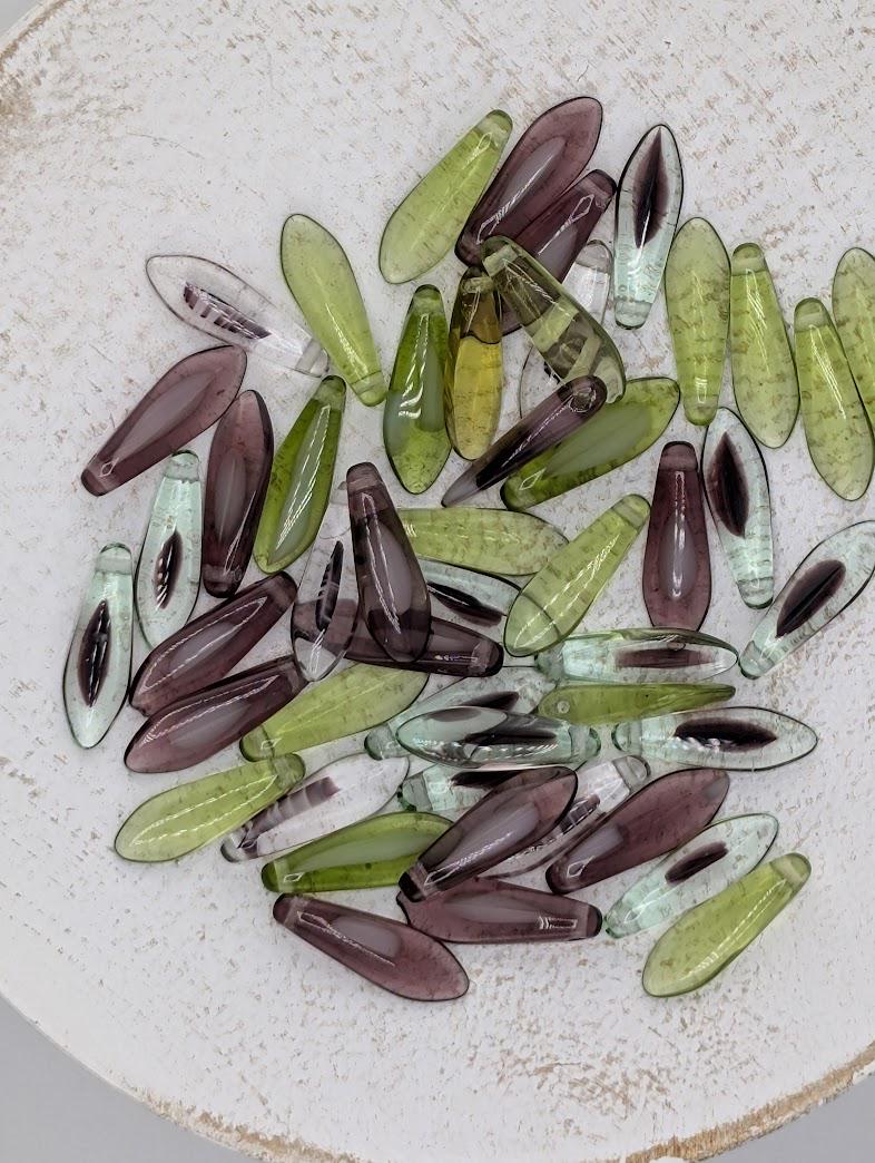 a collection of various colored glass beads, including green, purple, and clear beads, scattered on a white surface.