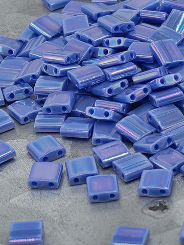 a pile of small, square-shaped blue beads on a surface.