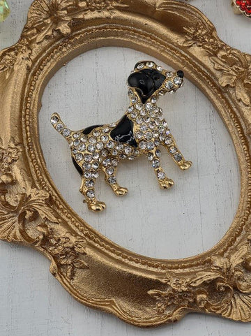 A decorative gold-framed brooch in the shape of a dog is displayed on a white surface.