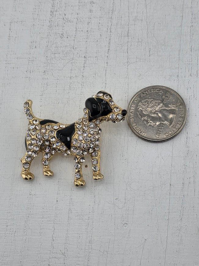 A decorative gold-framed brooch in the shape of a dog is displayed on a white surface.