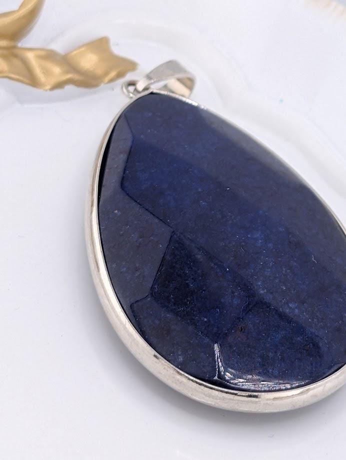 A close-up image of a large, dark blue gemstone pendant with a silver frame.