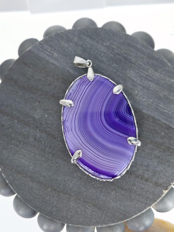 a large oval-shaped purple stone with a silver frame, displayed on a gray wooden surface.