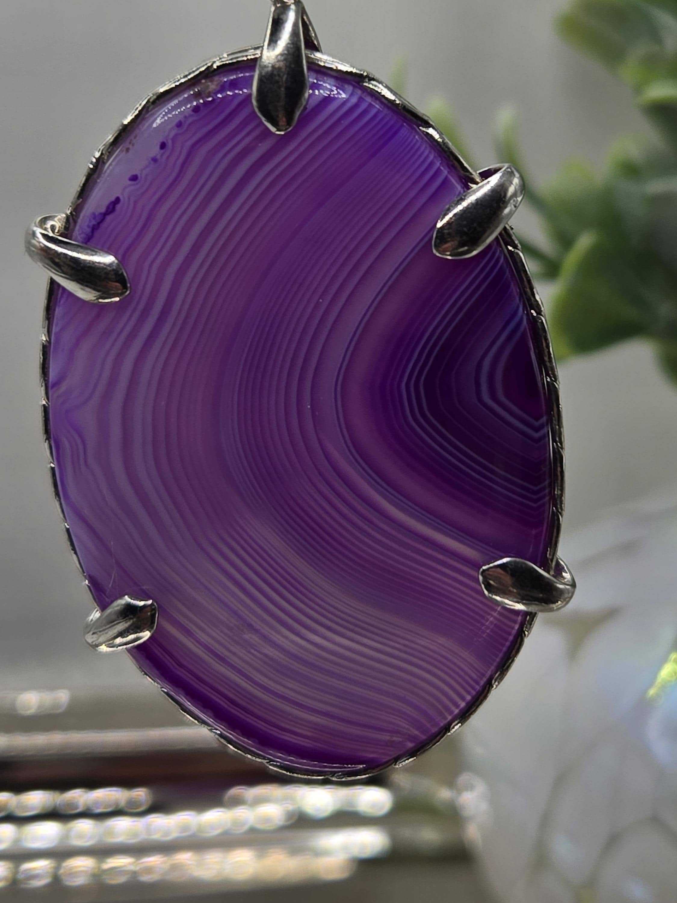 A close-up image of a purple stone with a unique striped pattern, mounted on a metal frame with metal claws.