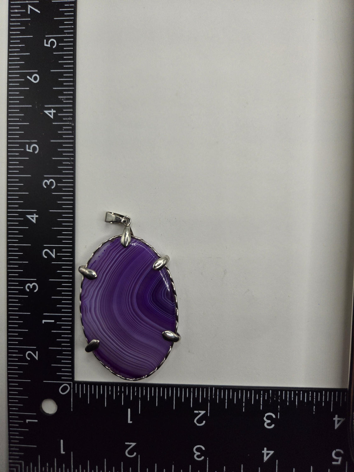 a purple stone pendant with a silver clasp, placed next to a ruler for size comparison.