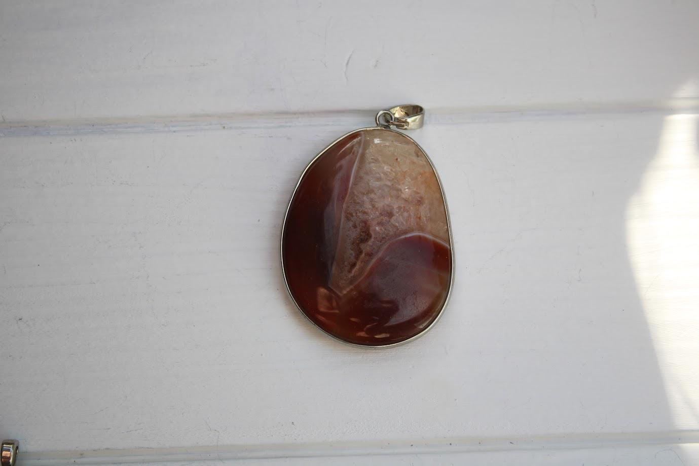 A pendant made of a large, irregularly shaped stone is hanging on a white wall.