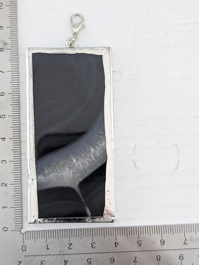 a rectangular black and silver pendant hanging from a chain.