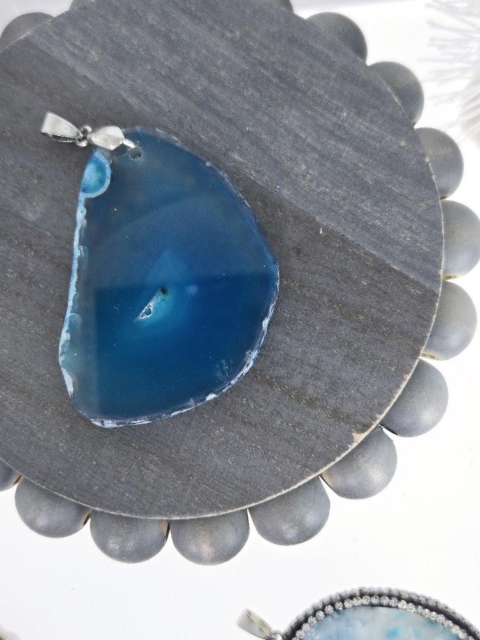 a blue agate stone with a silver pendant, placed on a gray circular surface.