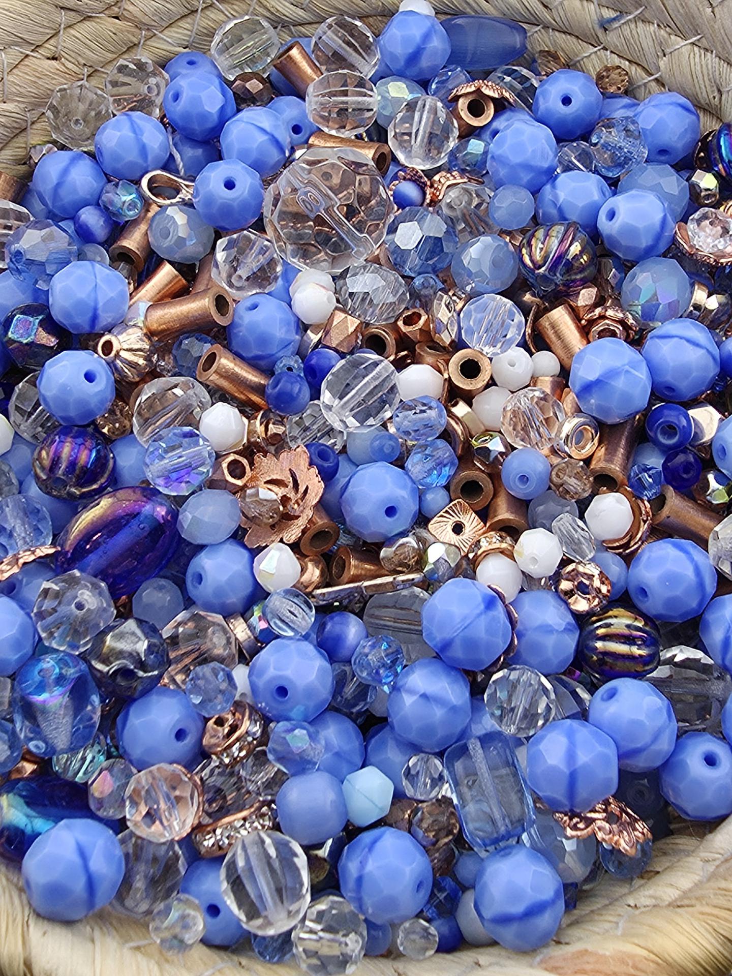 The image is a close-up of a collection of various blue and clear beads, including clear beads, blue beads, and copper-colored beads, all mixed together in a pile.