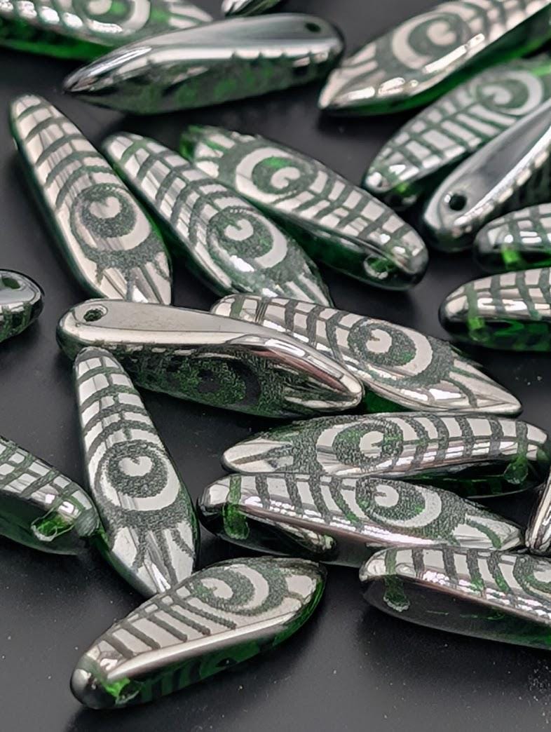 a collection of green and silver beads with intricate designs, scattered on a dark surface.