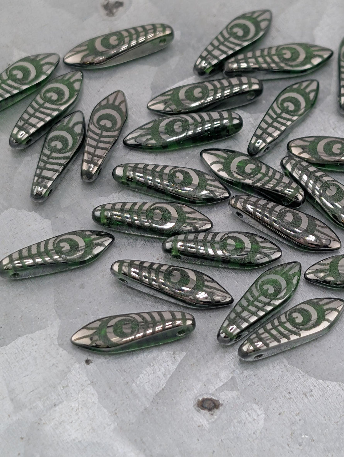 a collection of green and silver beads with intricate designs, scattered on a dark surface.
