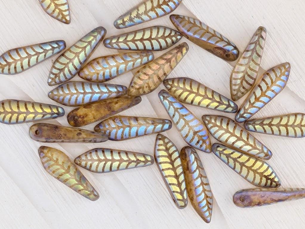 a collection of various colored glass beads with leaf-like patterns, scattered on a white surface.