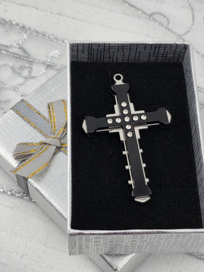 A black cross pendant with silver accents is displayed in a silver gift box with a yellow ribbon bow.