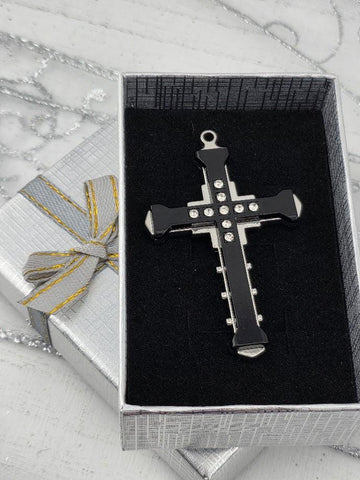 A black cross pendant with silver accents is displayed in a silver gift box with a yellow ribbon bow.