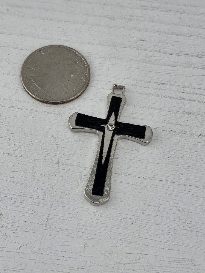 A silver cross pendant with a black interior is placed next to a US quarter on a white wooden surface.