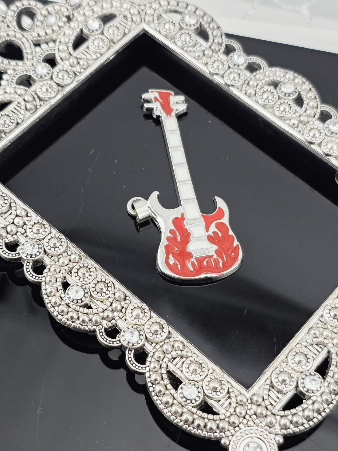 A close-up view of a red and silver guitar-shaped object, possibly a keychain or a decorative piece, placed on a black surface.