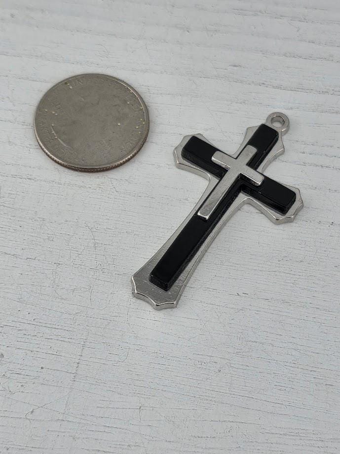 A silver cross-shaped pendant is placed next to a silver coin on a white surface.